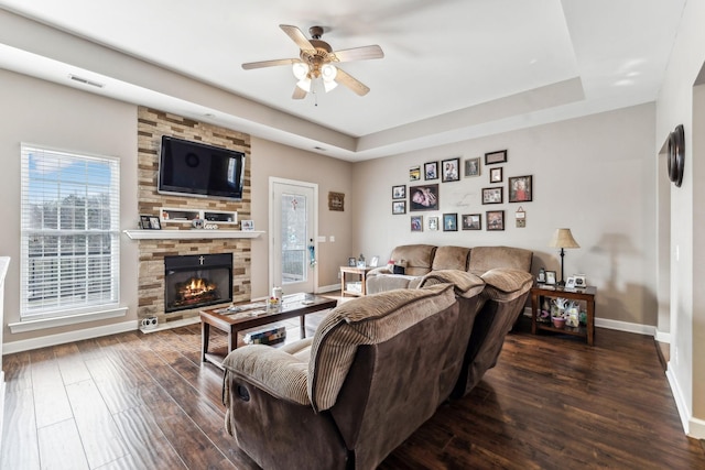 living room featuring ceiling fan, hardwood / wood-style flooring, a tray ceiling, and a stone fireplace