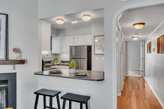 kitchen featuring kitchen peninsula, sink, light hardwood / wood-style flooring, white cabinets, and stainless steel fridge