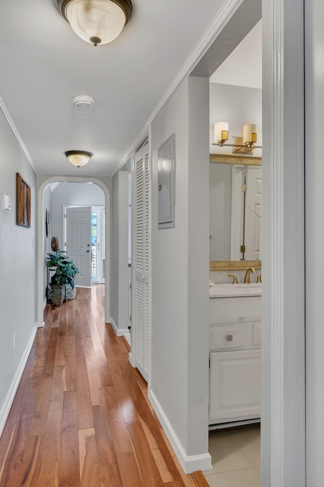 hall with crown molding, sink, electric panel, and light hardwood / wood-style flooring