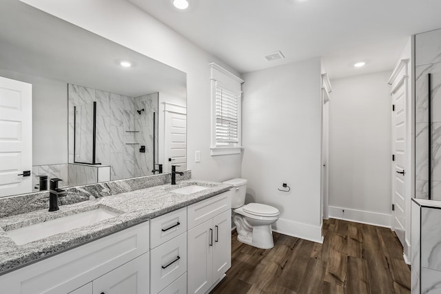 bathroom featuring a tile shower, hardwood / wood-style floors, vanity, and toilet