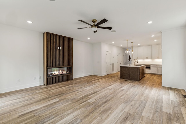 kitchen with light hardwood / wood-style floors, a center island with sink, ceiling fan, decorative light fixtures, and white cabinets