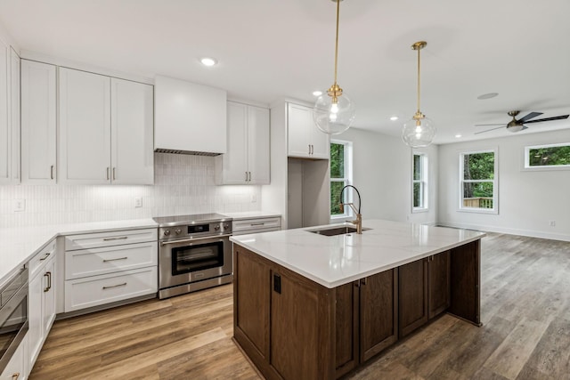 kitchen with sink, high end stainless steel range, white cabinets, and a center island with sink