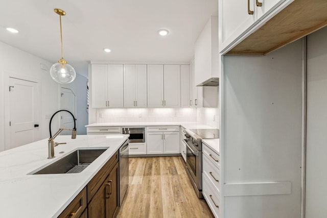 kitchen with white cabinets, stainless steel appliances, sink, hanging light fixtures, and light hardwood / wood-style flooring