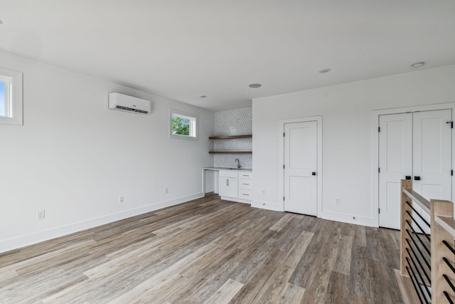 unfurnished living room with light hardwood / wood-style floors, sink, and a wall mounted AC