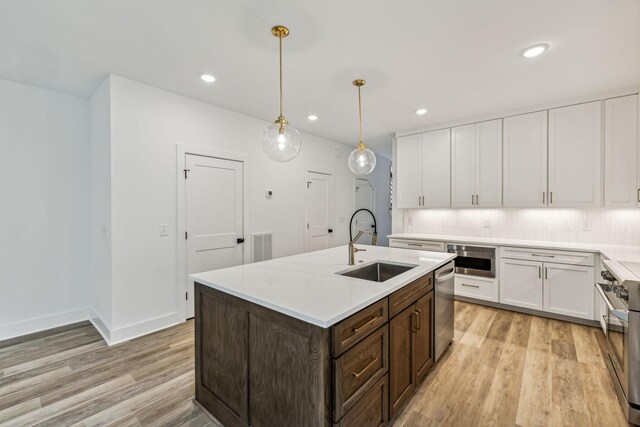 kitchen featuring a center island with sink, sink, hanging light fixtures, stainless steel appliances, and white cabinets