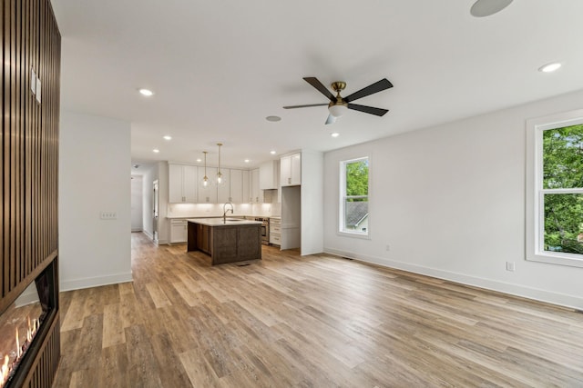 unfurnished living room featuring ceiling fan, a healthy amount of sunlight, light hardwood / wood-style floors, and sink