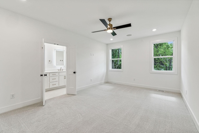 unfurnished bedroom with ceiling fan, sink, light carpet, and ensuite bath