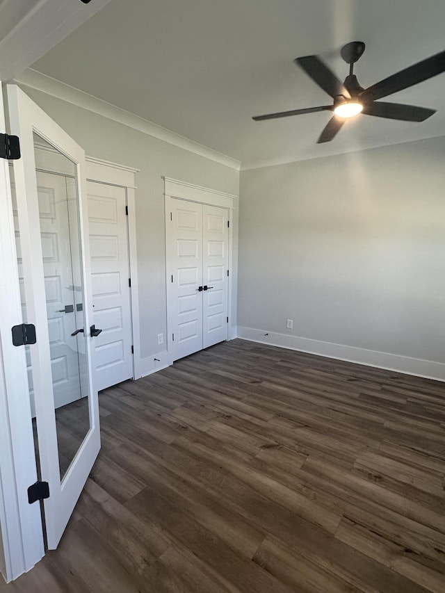 unfurnished bedroom with ceiling fan, multiple closets, dark wood-type flooring, and crown molding