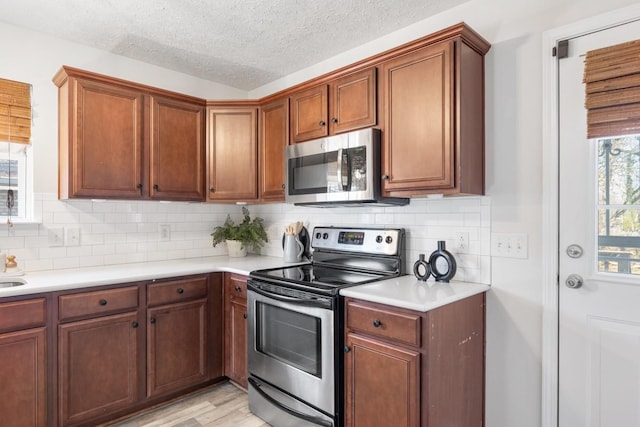 kitchen featuring decorative backsplash, appliances with stainless steel finishes, a textured ceiling, and light hardwood / wood-style floors