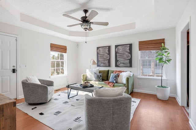 living room with a textured ceiling, ceiling fan, wood-type flooring, and a tray ceiling