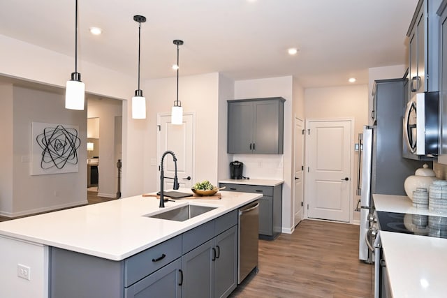 kitchen with gray cabinets, an island with sink, stainless steel appliances, pendant lighting, and sink