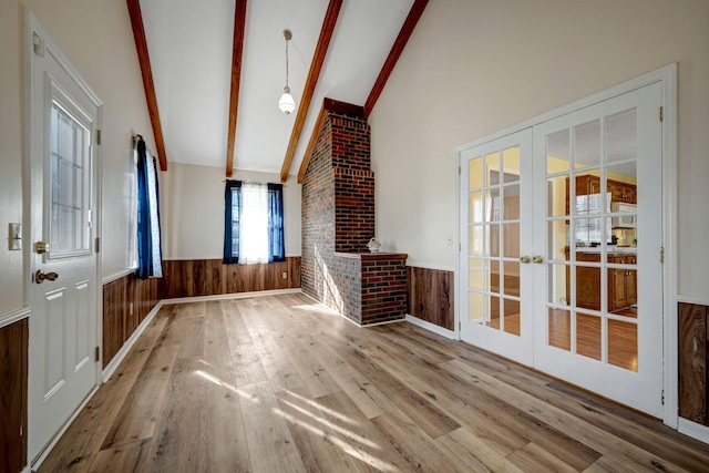 unfurnished living room featuring wood-type flooring, a fireplace, french doors, and lofted ceiling with beams