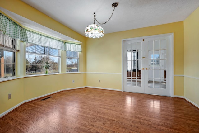 unfurnished dining area featuring wood-type flooring, a notable chandelier, french doors, and a textured ceiling