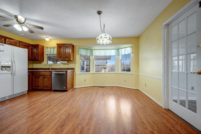 kitchen featuring ceiling fan with notable chandelier, pendant lighting, dishwasher, white refrigerator with ice dispenser, and light hardwood / wood-style flooring