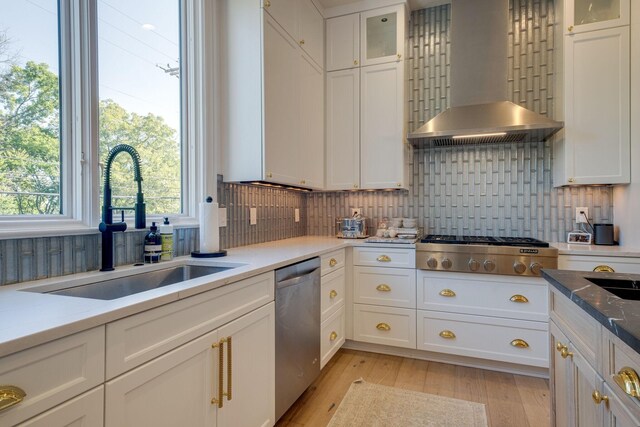 kitchen featuring stainless steel appliances, sink, white cabinetry, and wall chimney range hood