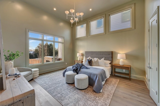 bedroom featuring light hardwood / wood-style floors, a towering ceiling, and a chandelier