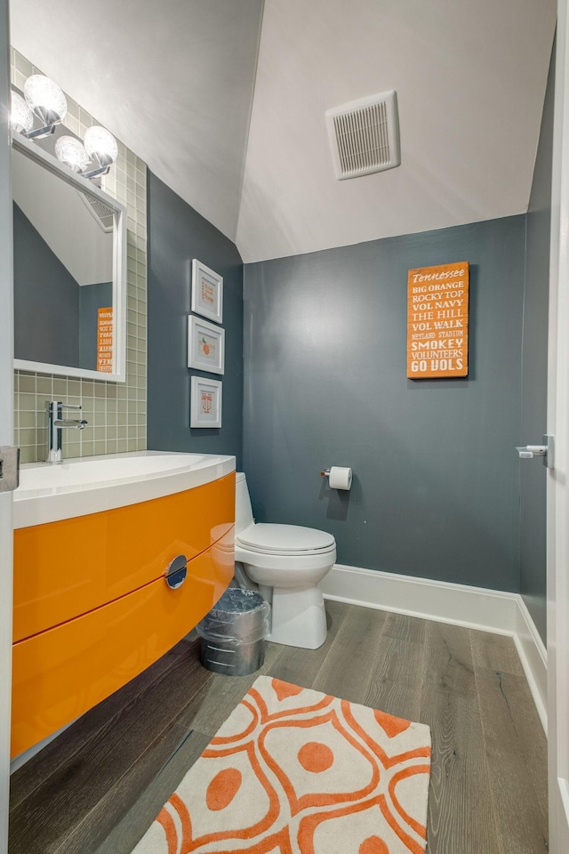 bathroom with toilet, backsplash, lofted ceiling, wood-type flooring, and vanity