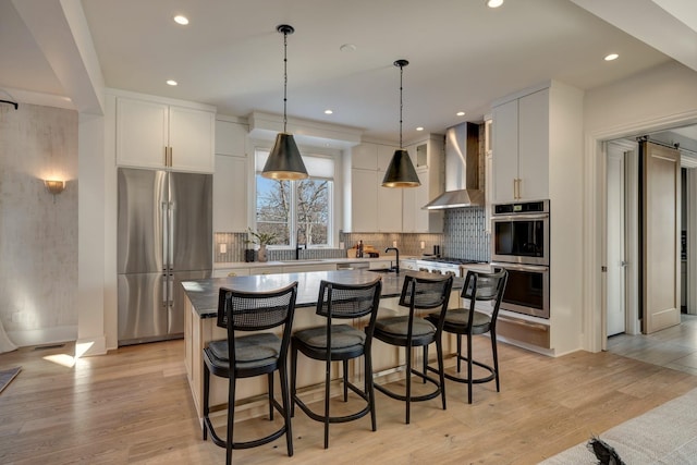 kitchen with white cabinets, hanging light fixtures, appliances with stainless steel finishes, and wall chimney exhaust hood