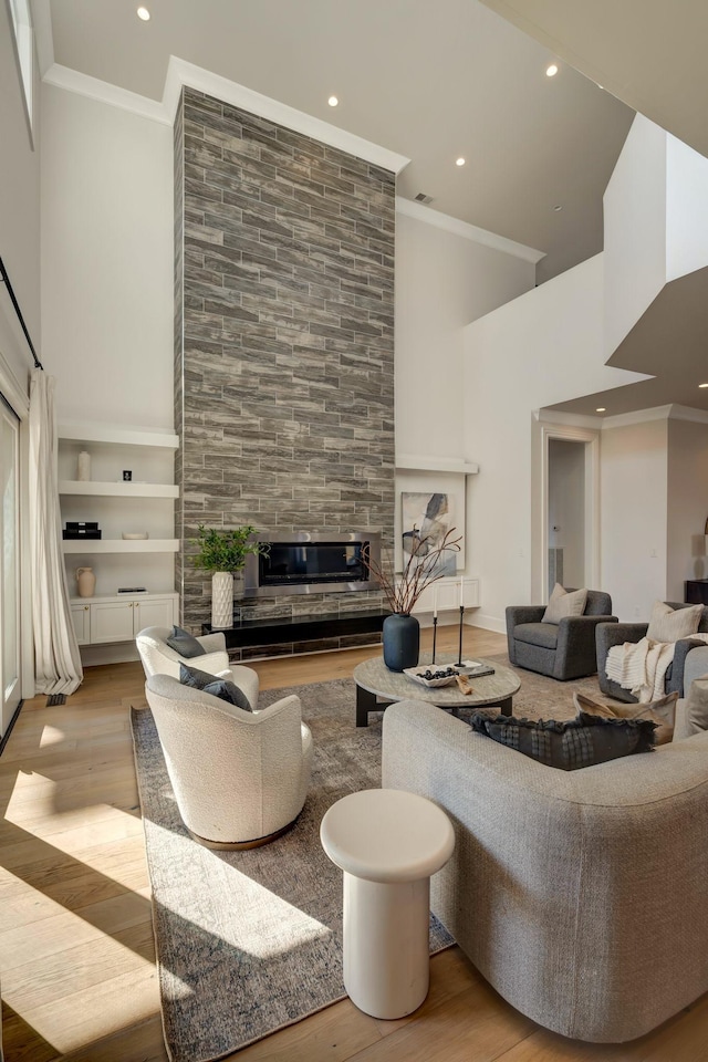 living room with ornamental molding, a fireplace, light hardwood / wood-style flooring, and built in shelves