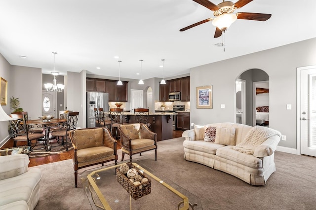 carpeted living room with ceiling fan with notable chandelier