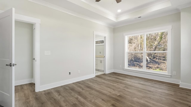 unfurnished bedroom with ensuite bathroom, ceiling fan, a tray ceiling, dark hardwood / wood-style flooring, and ornamental molding