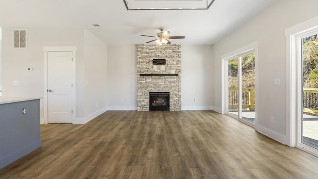 unfurnished living room featuring ceiling fan, dark hardwood / wood-style flooring, and a stone fireplace