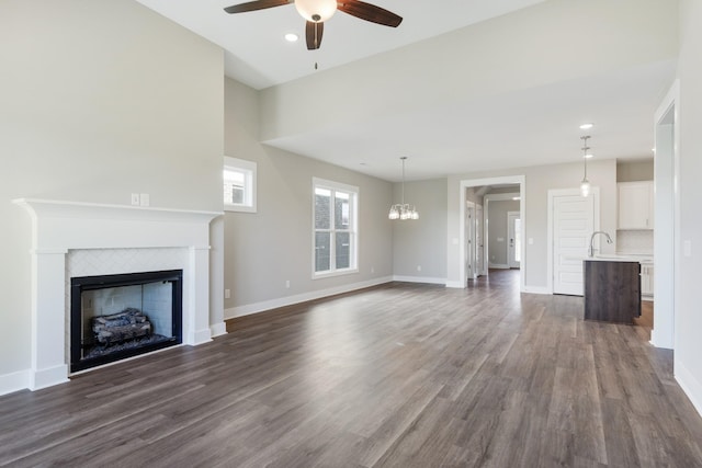 unfurnished living room featuring ceiling fan with notable chandelier, sink, dark hardwood / wood-style flooring, and a fireplace