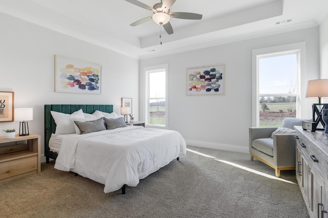 carpeted bedroom featuring ceiling fan, a raised ceiling, visible vents, and baseboards