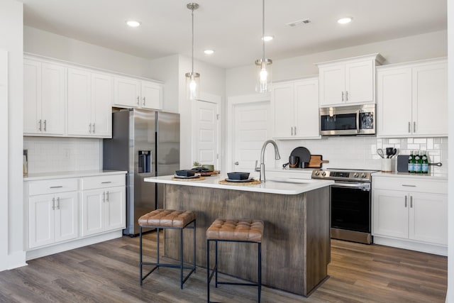 kitchen featuring a center island with sink, appliances with stainless steel finishes, decorative light fixtures, light countertops, and white cabinetry