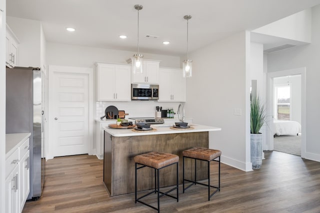 kitchen featuring a center island with sink, white cabinetry, stainless steel appliances, and light countertops