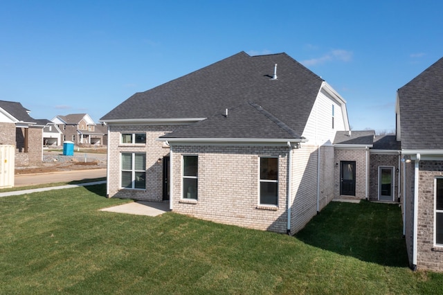 rear view of house featuring brick siding, a lawn, and roof with shingles