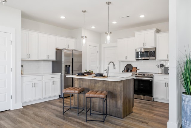 kitchen with an island with sink, stainless steel appliances, light countertops, white cabinetry, and a sink