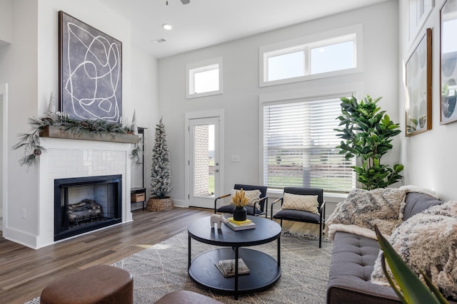 living area with visible vents, baseboards, a tile fireplace, a towering ceiling, and dark wood-type flooring