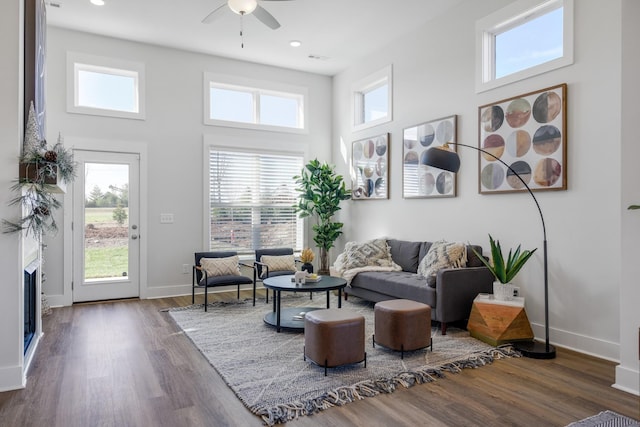 living room featuring dark wood-type flooring, a fireplace, a towering ceiling, and baseboards