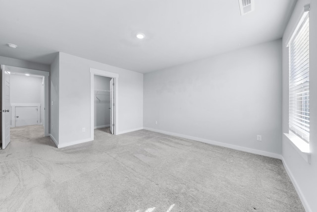 unfurnished bedroom featuring a walk in closet, a closet, and light colored carpet