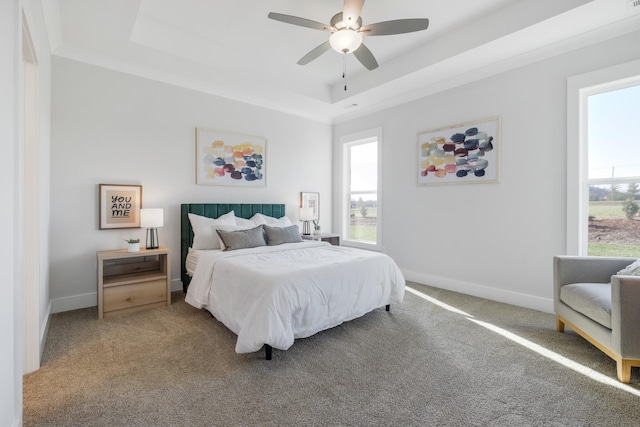 carpeted bedroom with ceiling fan, multiple windows, and a tray ceiling