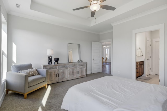 bedroom with ceiling fan with notable chandelier, connected bathroom, light carpet, ornamental molding, and a raised ceiling