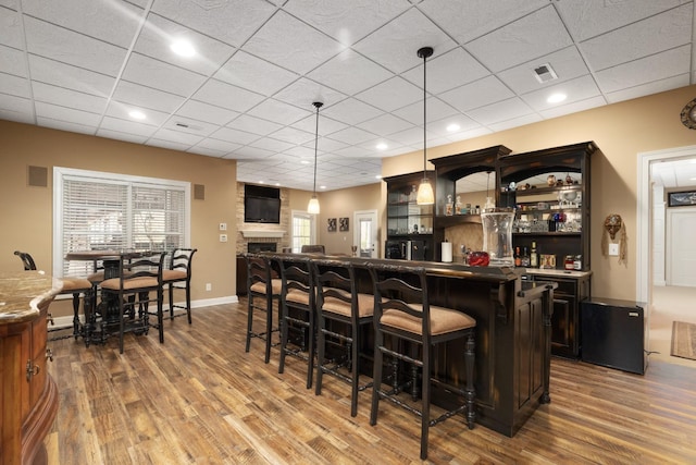 bar with a paneled ceiling, a fireplace, hardwood / wood-style flooring, and decorative light fixtures