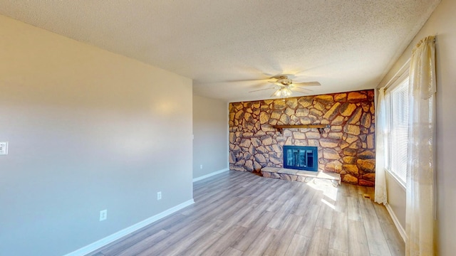 unfurnished living room with ceiling fan, light wood-type flooring, a stone fireplace, and a textured ceiling