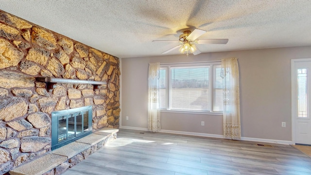 unfurnished living room featuring ceiling fan, a textured ceiling, light hardwood / wood-style flooring, and a stone fireplace