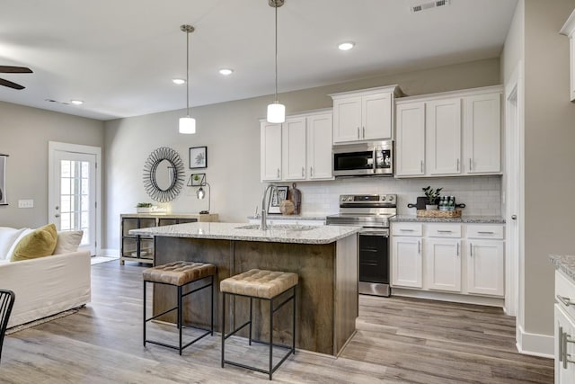 kitchen featuring decorative backsplash, appliances with stainless steel finishes, white cabinetry, and a center island with sink