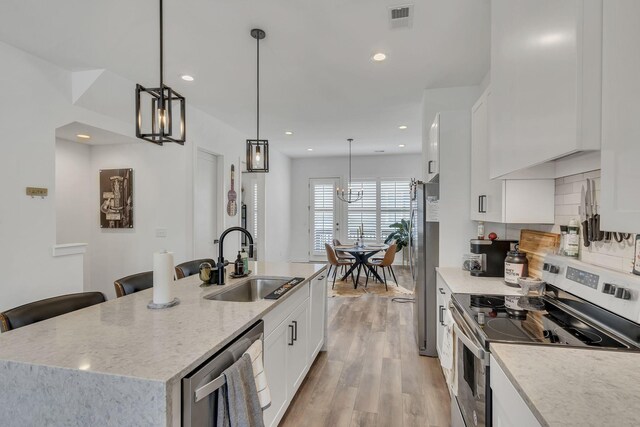 kitchen featuring white cabinets, appliances with stainless steel finishes, decorative light fixtures, sink, and a center island with sink