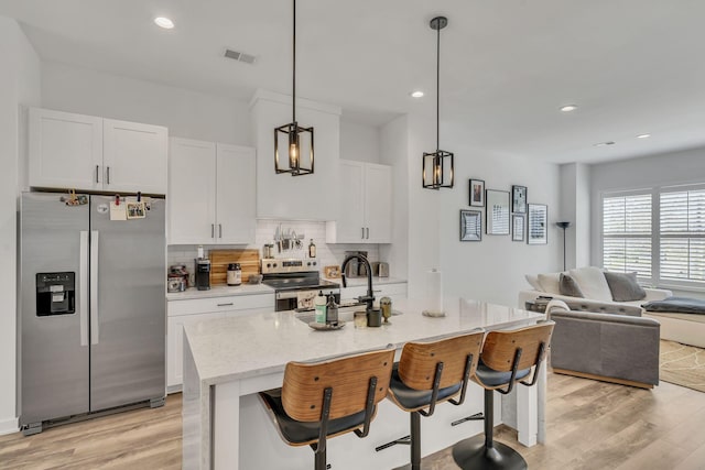 kitchen featuring white cabinetry, stainless steel appliances, a breakfast bar area, and an island with sink