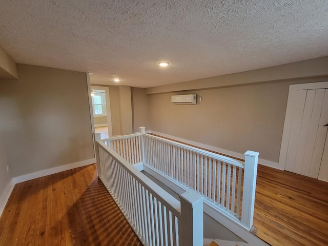 corridor with a wall unit AC, a textured ceiling, and hardwood / wood-style flooring