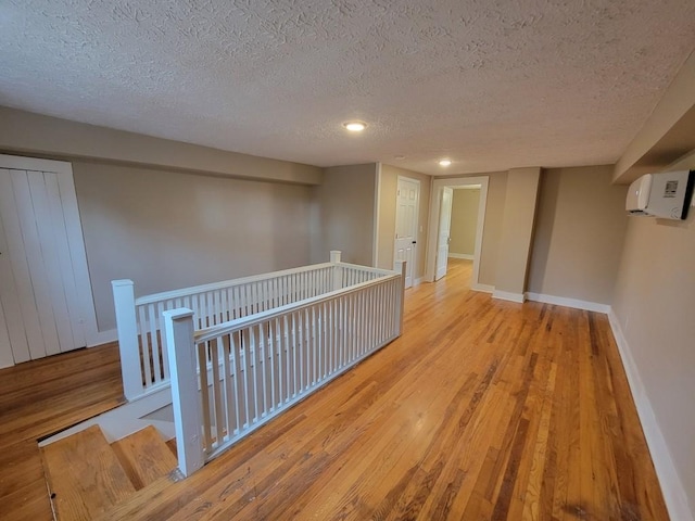 hall featuring an AC wall unit, a textured ceiling, and light hardwood / wood-style floors