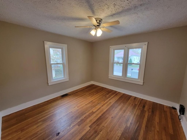 empty room with a wealth of natural light, a textured ceiling, and hardwood / wood-style floors