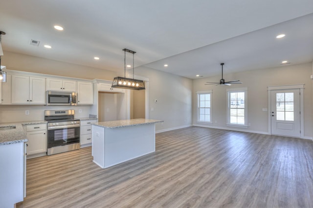 kitchen featuring appliances with stainless steel finishes, a kitchen island, white cabinetry, hanging light fixtures, and ceiling fan