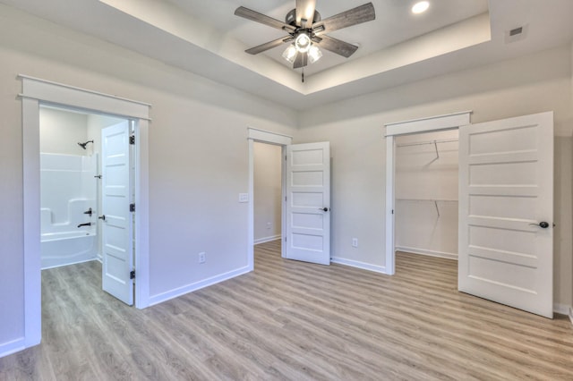 unfurnished bedroom featuring a spacious closet, ceiling fan, a raised ceiling, a closet, and light hardwood / wood-style flooring