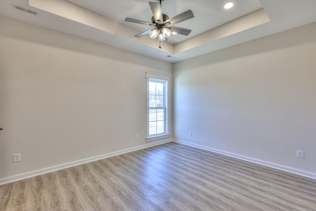 unfurnished room featuring a raised ceiling, light wood-type flooring, and ceiling fan