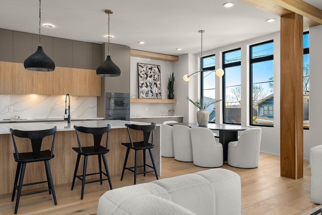 kitchen with a breakfast bar area, decorative backsplash, light hardwood / wood-style flooring, and decorative light fixtures